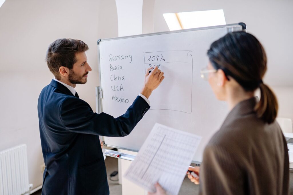 Business professionals in a meeting discussing strategies on a whiteboard.
