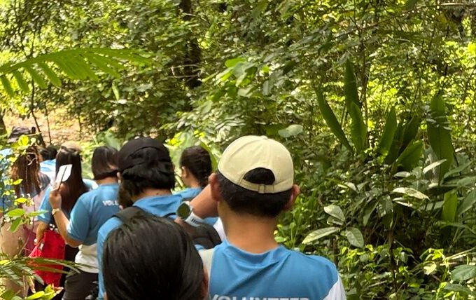 Sourcefit volunteers in blue volunteer shirts walking single file along a forest trail