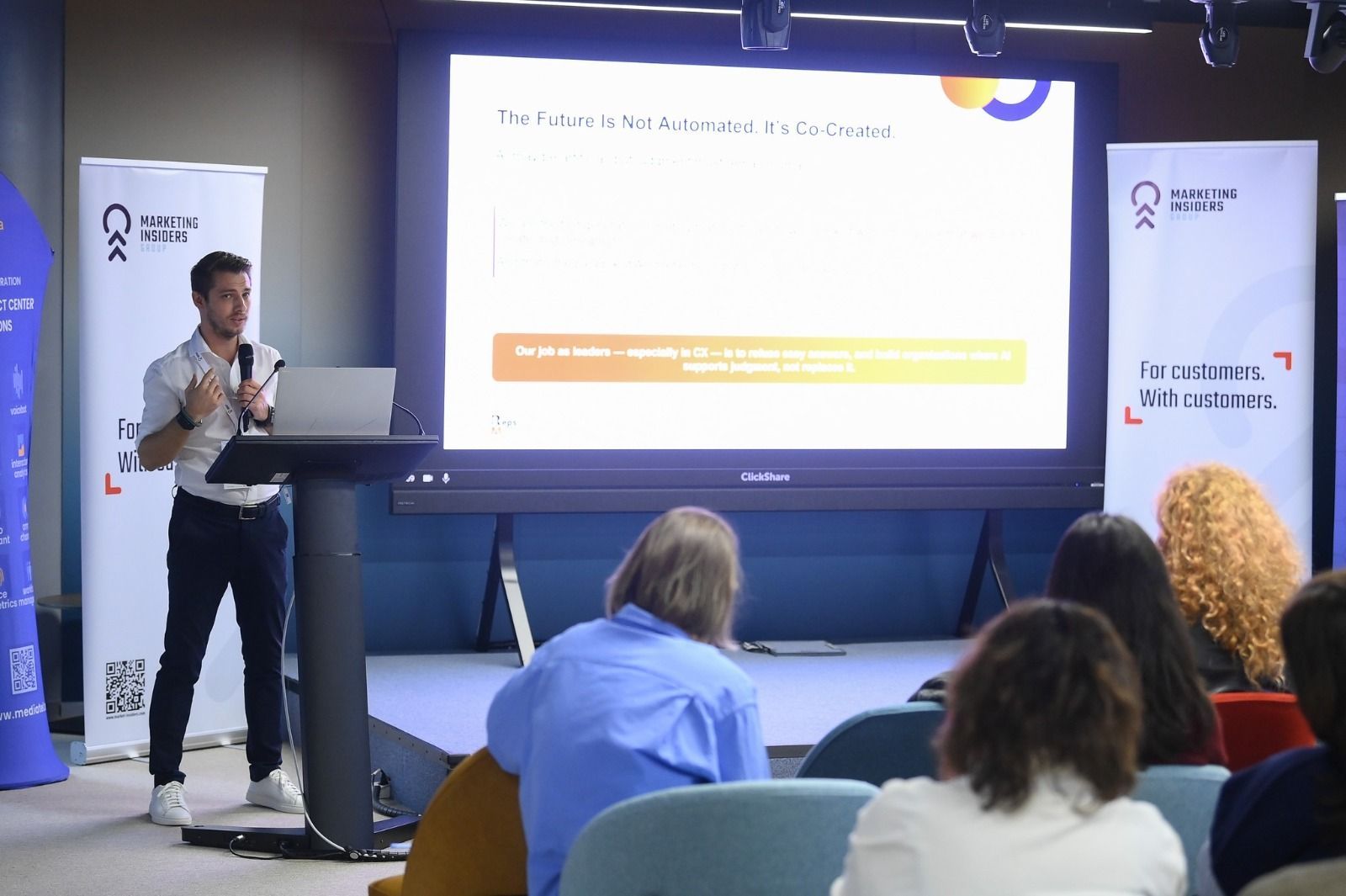 Alin Roșca speaking at a podium beside a slide headed The Future Is Not Automated. It