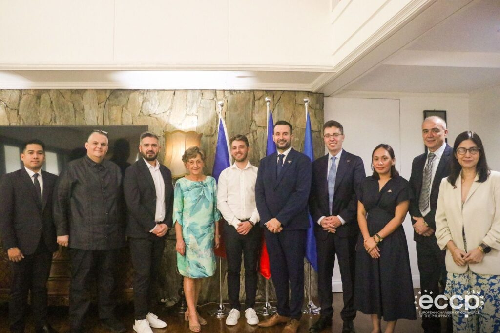 Alin Roșca standing with ten guests in front of a stone wall and flags at the partnership signing